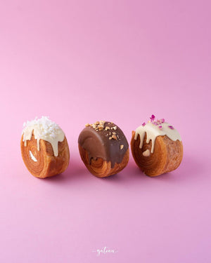 Gateau Gourmet Cafe gourmet croissant rolls with white, chocolate, and vanilla icing on pink background