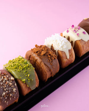 Assorted gourmet croissant rolls topped with pistachio, chocolate crumble, coconut, and white chocolate drizzle