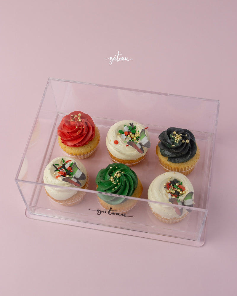 Assorted gourmet cupcakes in red, green, black, and white frosting in a clear box from Gateau Gourmet Cafe for gourmet cupcakes delivery