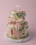 Two-tier gourmet fionka cake with pastel pink bow and green floral decorations by Gateau Gourmet Cafe