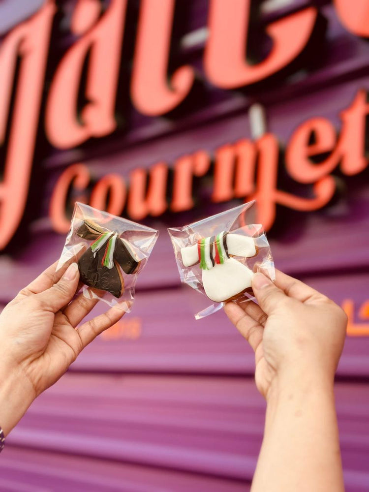 Two National Day themed cookies UAE in clear packaging held up against the Gateau Gourmet Cafe backdrop