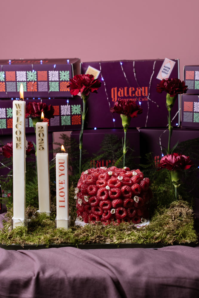 Gourmet raspberry cake arrangement presented with candles and flowers at Gateau Gourmet Cafe