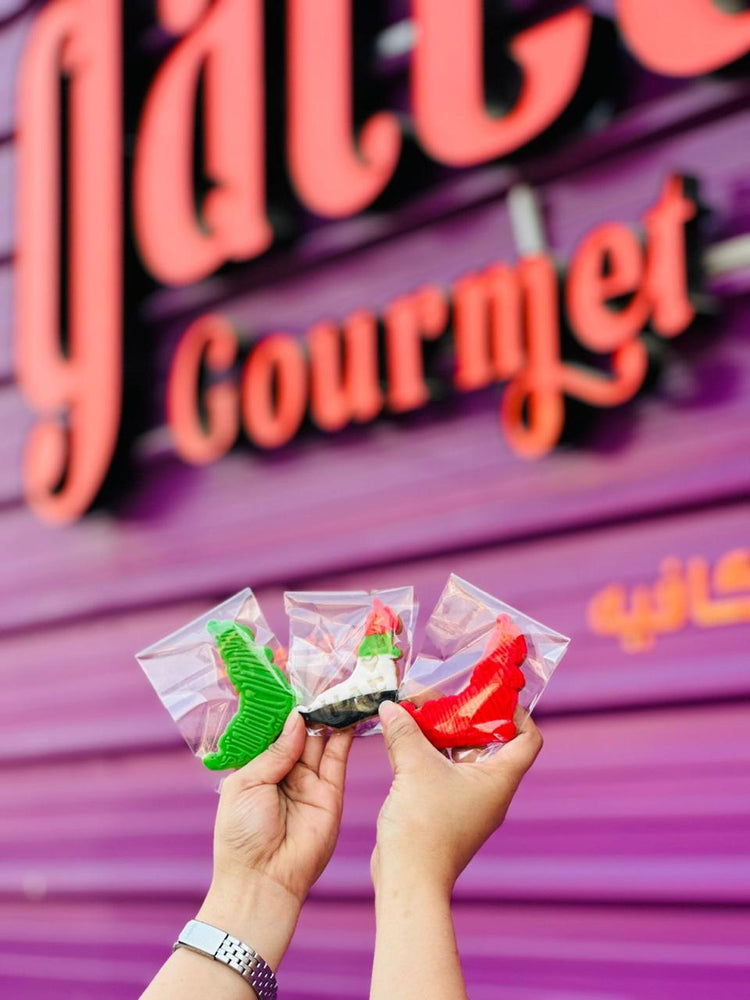 Hand holding colorful UAE National Day cookies from Gateau Gourmet Cafe on a vibrant background