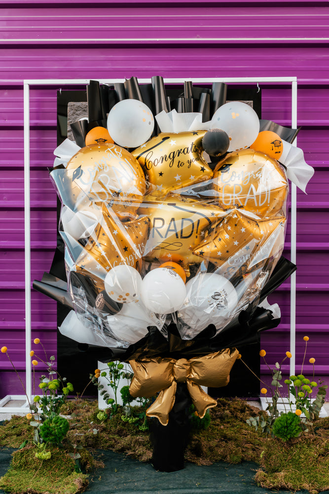 A vibrant graduation balloons bouquet featuring gold and black balloons with celebratory messages for graduation parties