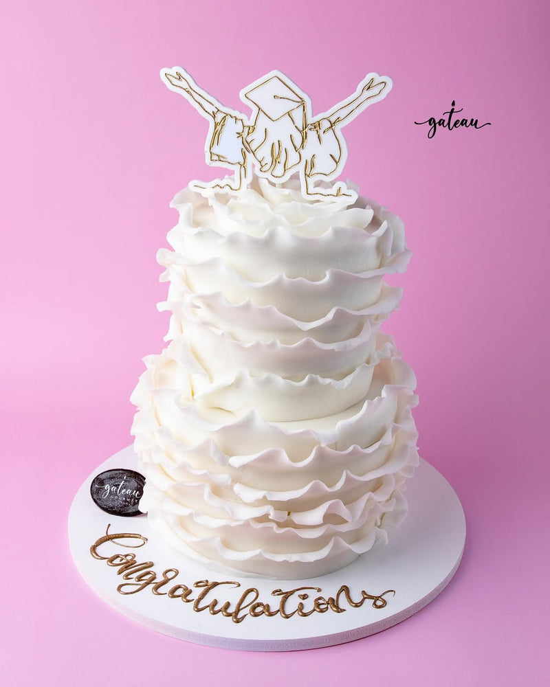 White tiered cake with ruffled icing and graduation cap topper for graduation cake ideas
