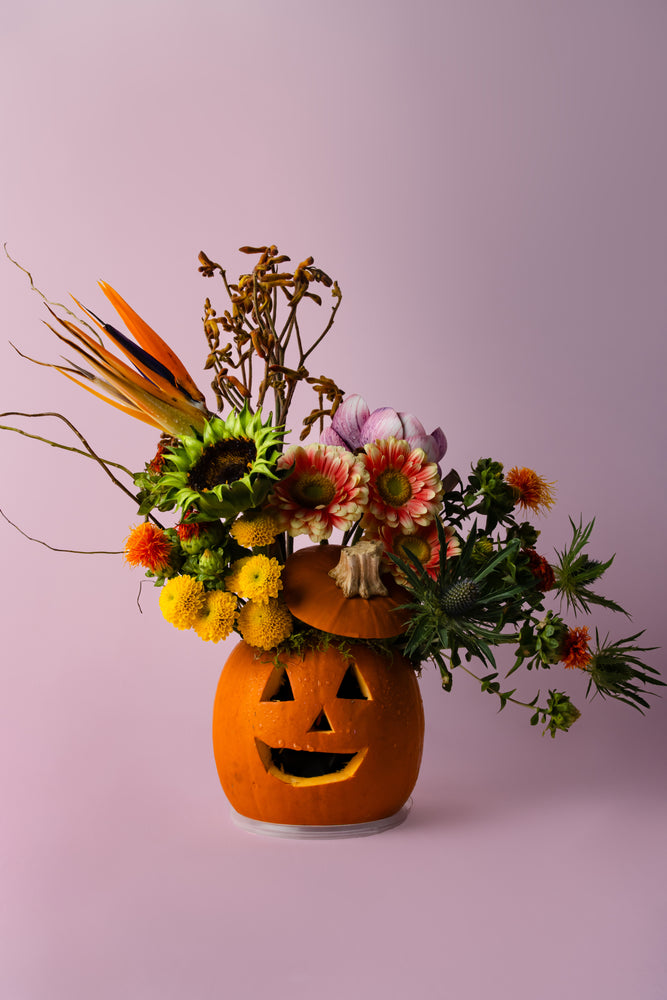 Halloween pumpkin flower arrangement featuring colorful flowers and autumn foliage in a carved pumpkin vase