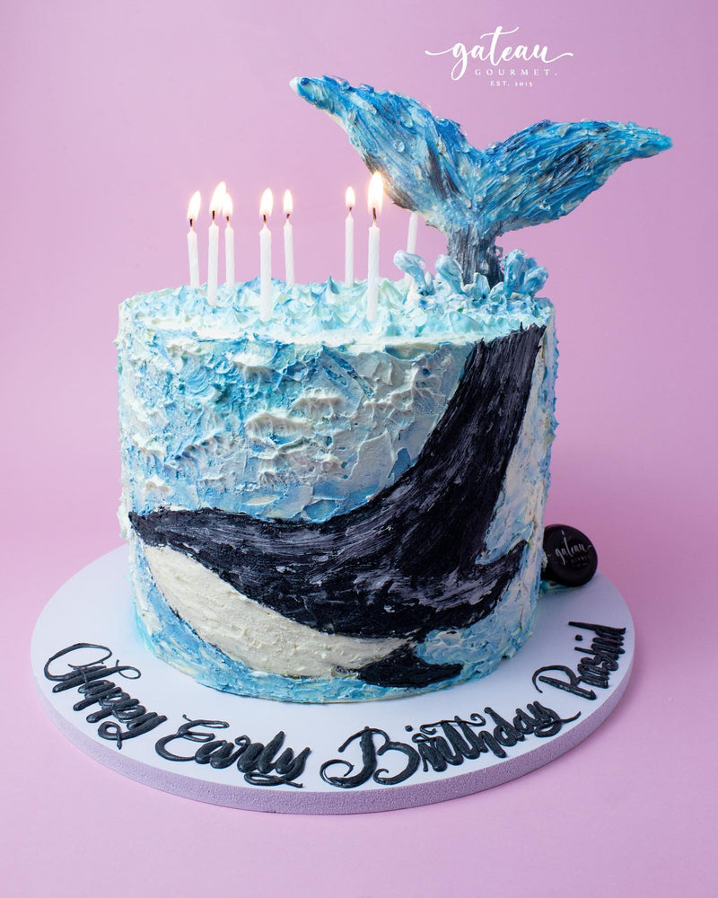 Hand-painted whale cake with vibrant blue frosting and decorative candles for a birthday celebration