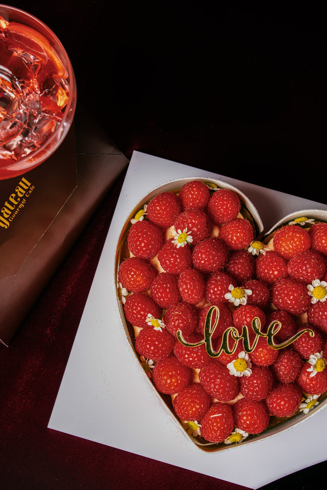 Heart shape raspberry tart topped with fresh raspberries and decorative flowers from Gateau Gourmet Cafe