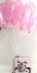 Pink helium balloons for parties tied to a clear gift box with flowers inside from Gateau Gourmet Cafe