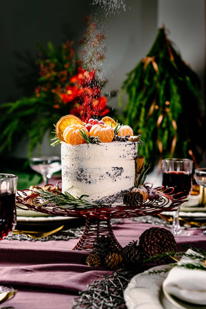Holiday gourmet cake by Gateau Gourmet Cafe decorated with citrus and pine cones on festive table