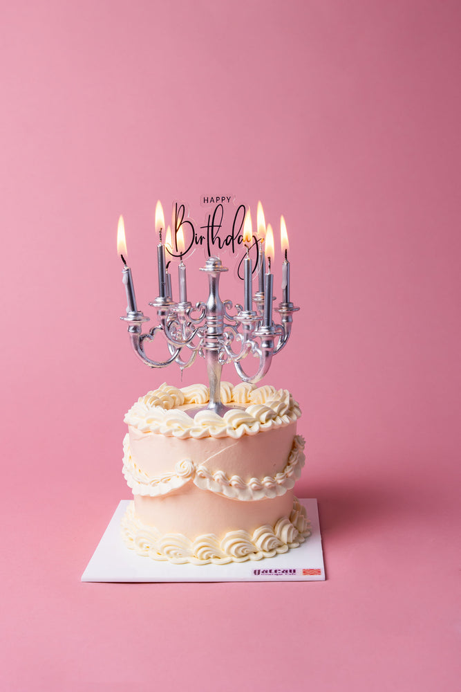 Gateau Gourmet Cafe Lumiere birthday cake with elegant white frosting and lit candles on pink background