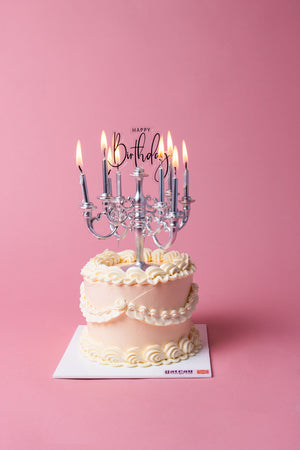 Gateau Gourmet Cafe Lumiere birthday cake with elegant white frosting and lit candles on pink background