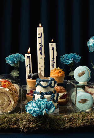 Ramadan dessert tray from Gateau Gourmet Cafe featuring assorted cakes, macarons, and decorative candles with blue flowers