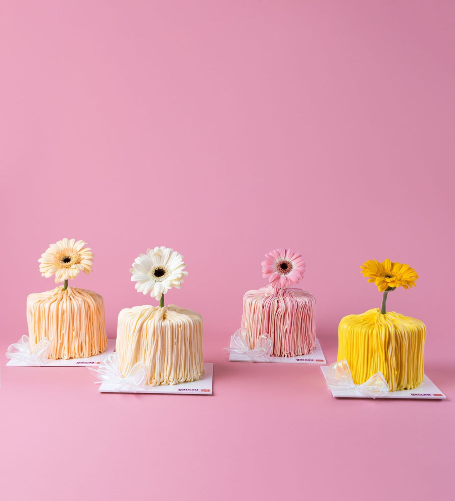 Mini Cake with Fresh Gerbera Flower in pastel colors by Gateau Gourmet Cafe on a pink background