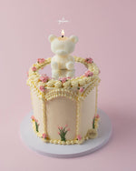 Mirror cake with bear candle topped with cream frosting and pink flower decorations by Gateau Gourmet Cafe