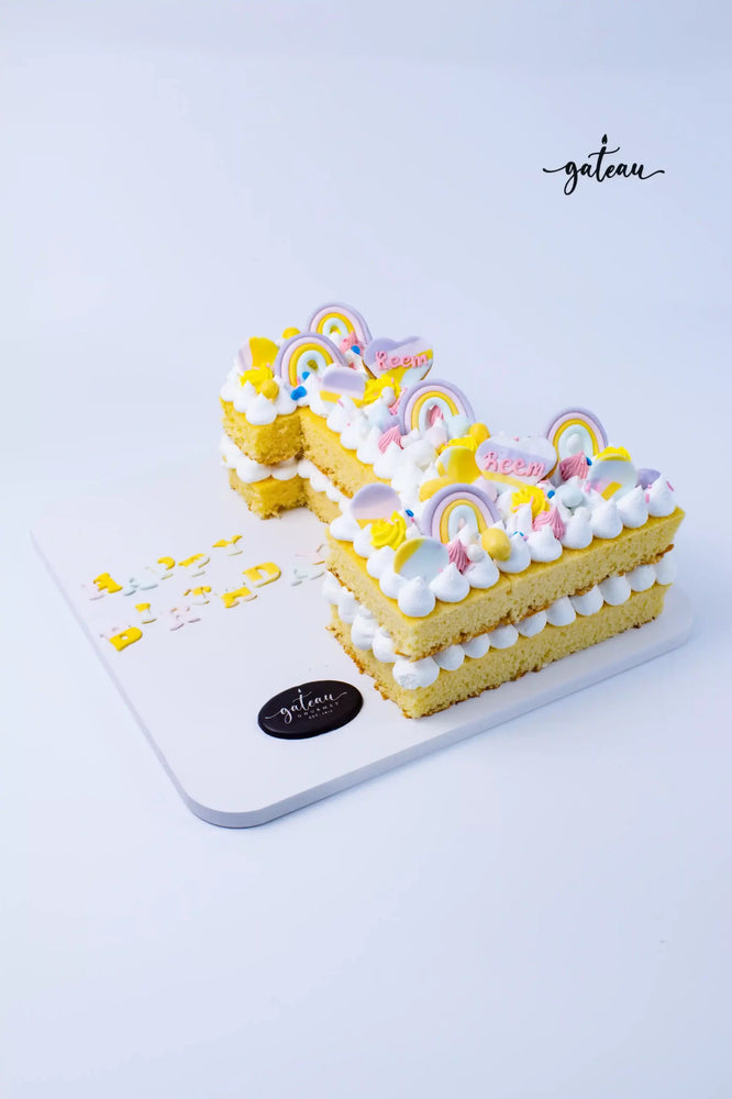 Number shaped birthday cake with rainbow and cloud decorations by Gateau Gourmet Cafe