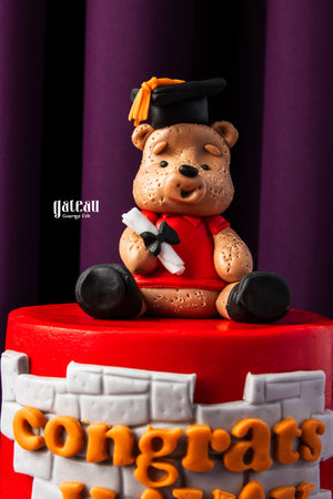 Personalized grad cake with name featuring a bear in graduation cap and gown sitting on a red cake