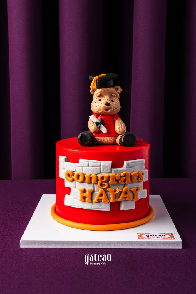 Personalized grad cake with name featuring a red base and a bear topper wearing a graduation cap
