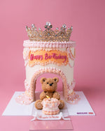 Princess crown cake for girls with pink and white frosting, a gold crown topper, and teddy bear decoration