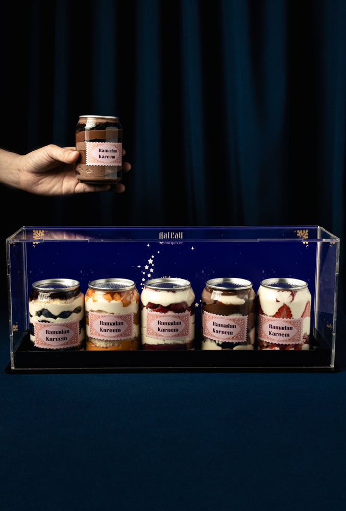 Gourmet canned cake jars from Gateau Gourmet Cafe displayed in a clear case with one held in hand