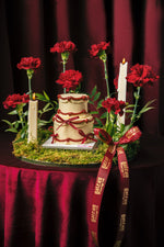 Gateau Gourmet Cafe red ribbon cake arrangement with cream cake, red carnations, and lit candles on a moss base