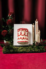 Red shimmer canvas cake with red frosting decorations displayed on an easel by Gateau Gourmet Cafe