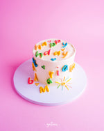 Scrabbled birthday mini cake decorated with colorful letters and cheerful designs on a pink background