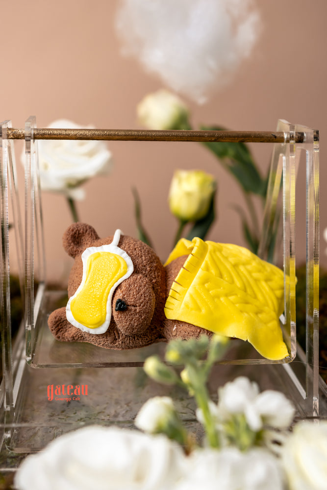Cute sleeping bear cake arrangement with a cozy yellow blanket and soft textures from Gateau Gourmet Cafe