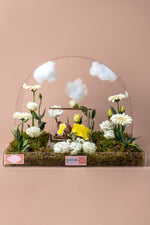Sleeping bear cake arrangement featuring edible flowers and a charming bear figure on a decorative base