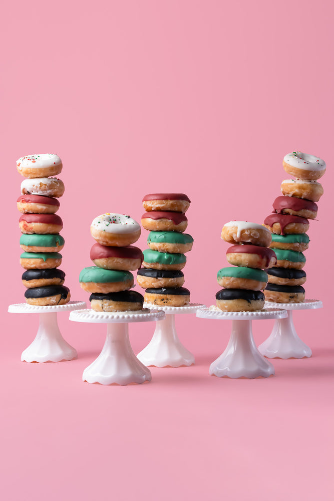 Stacked specialty flavored donuts in various colors and sprinkles on white stands by Gateau Gourmet Cafe