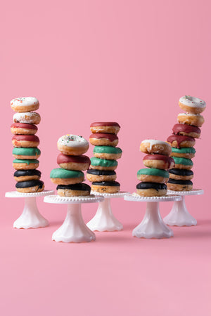 Stacked specialty flavored donuts in various colors and sprinkles on white stands by Gateau Gourmet Cafe