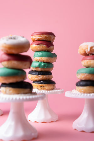 Stack of Gateau Gourmet Cafe specialty flavored donuts with colorful icing on white cake stands