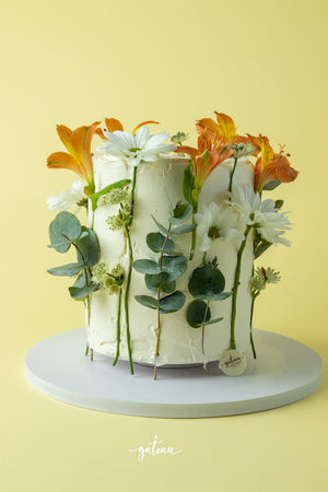Summer colors flowery cake decorated with fresh flowers and foliage on a light yellow background