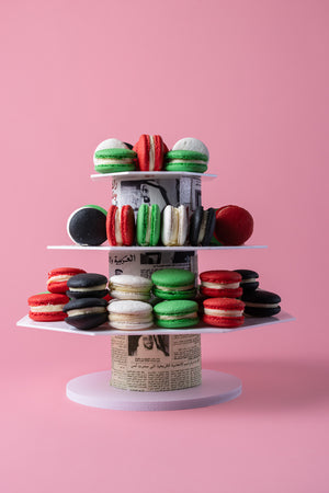 Colorful UAE colors macaroons displayed elegantly on a tiered stand against a pink background