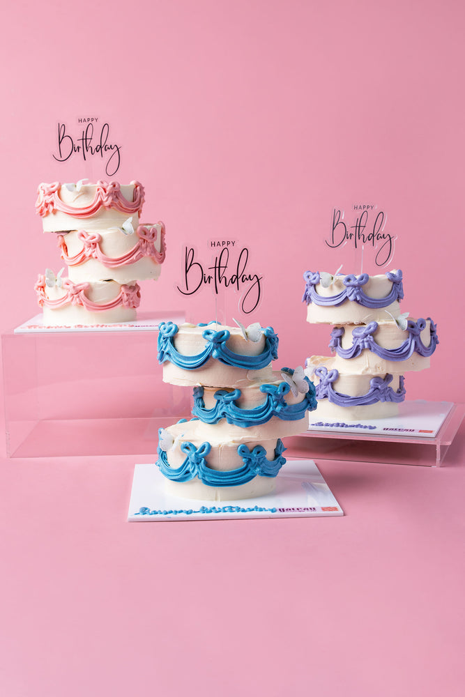 Three tiered cakes with pink, blue, and purple icing decorations showcasing unique birthday cake designs by Gateau Gourmet Cafe