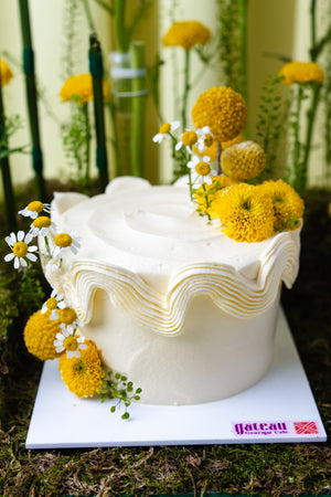 Gateau Gourmet Cafe white frosted cake with unique summer cake design featuring yellow flowers and intricate piping