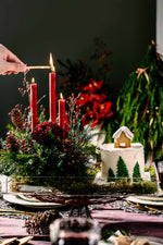 White Christmas Cake Design with Arrangement featuring a festive cake with pine tree decorations and a cozy holiday centerpiece with red candles and pinecones